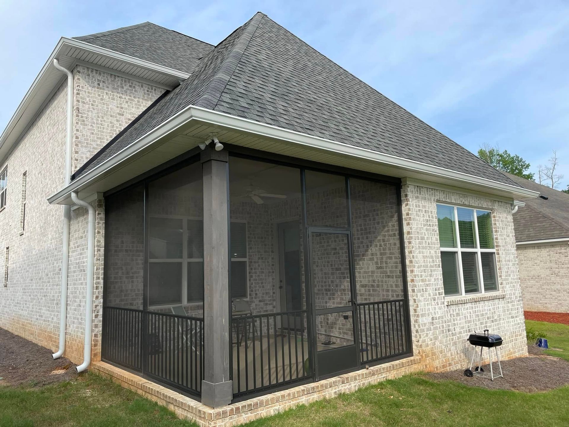 Screened back porch on a beige house with gray roof and black railings