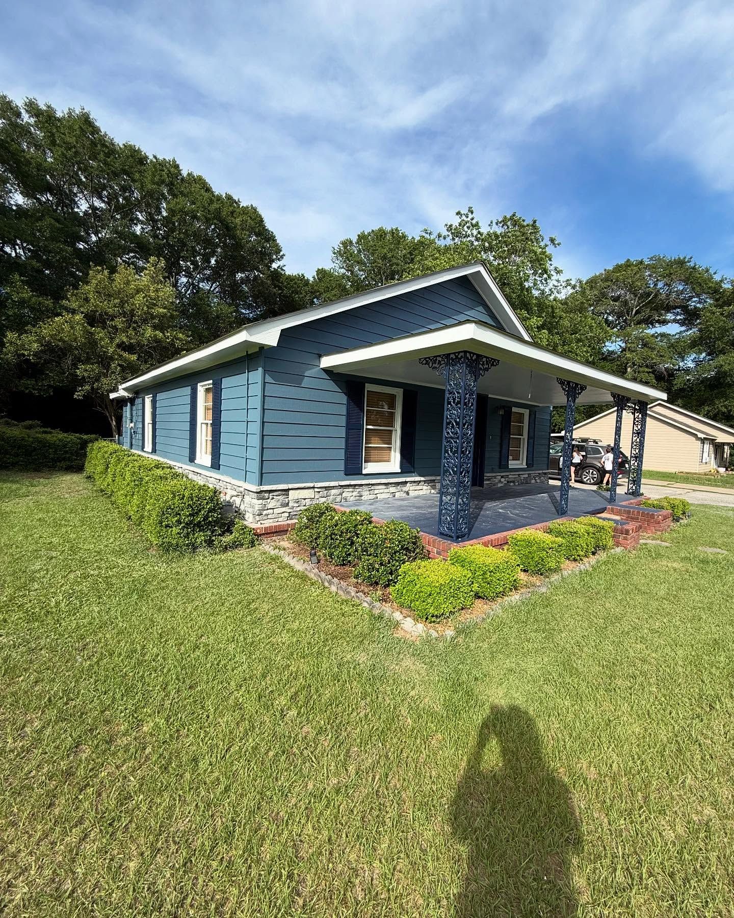 Small blue house with a covered front porch and a grassy yard under a partly cloudy sky