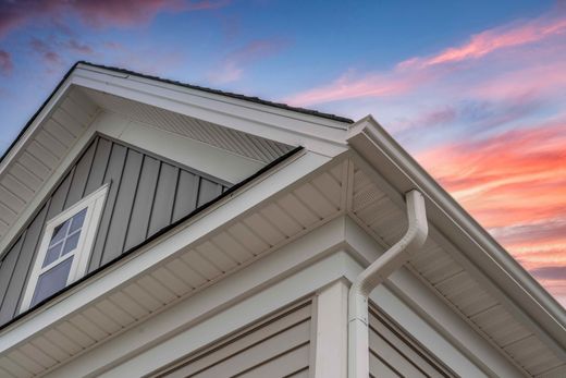 White house roof and siding with rain gutter against a pink sunset sky