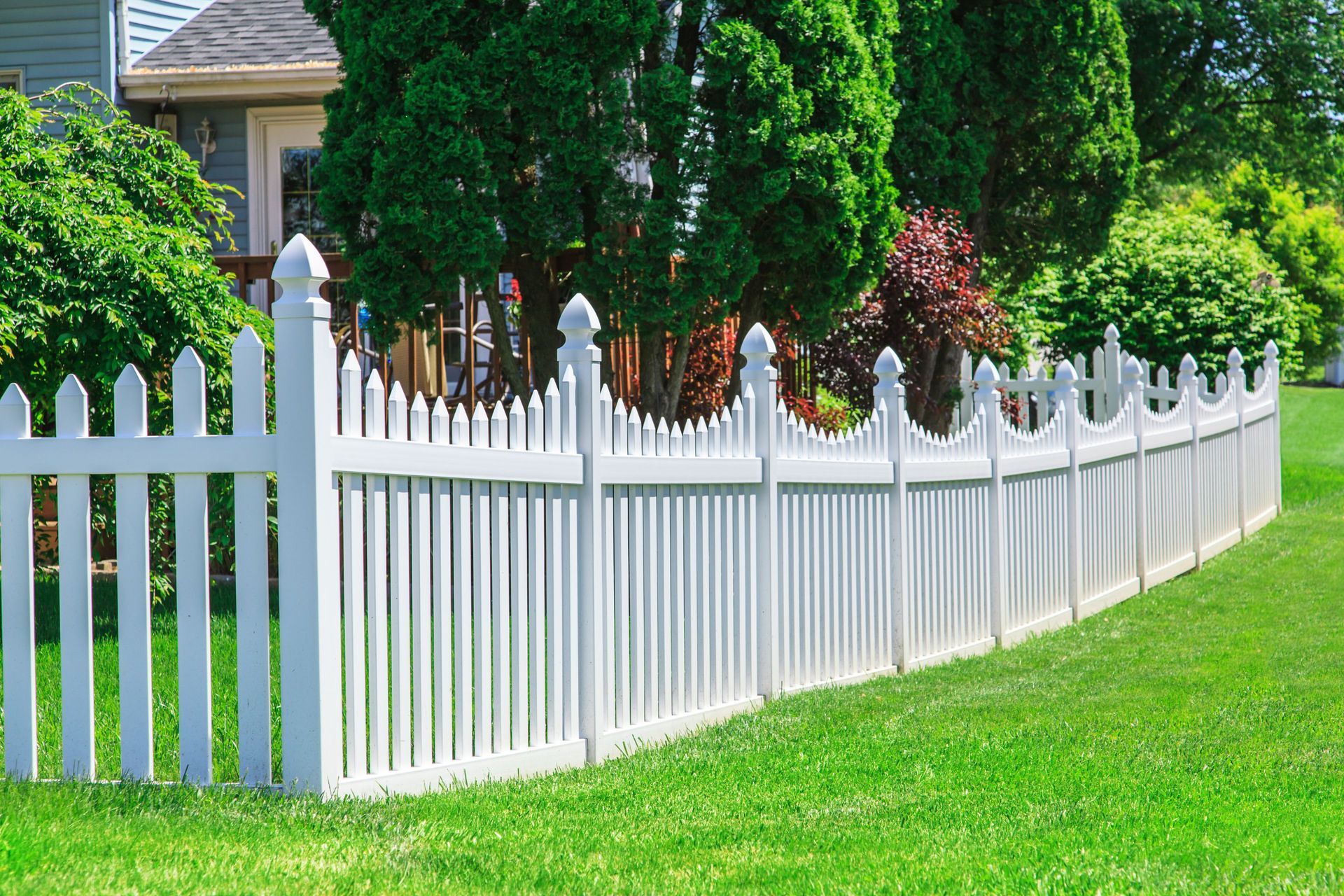 White picket fence curving along a green lawn beside a house and trees