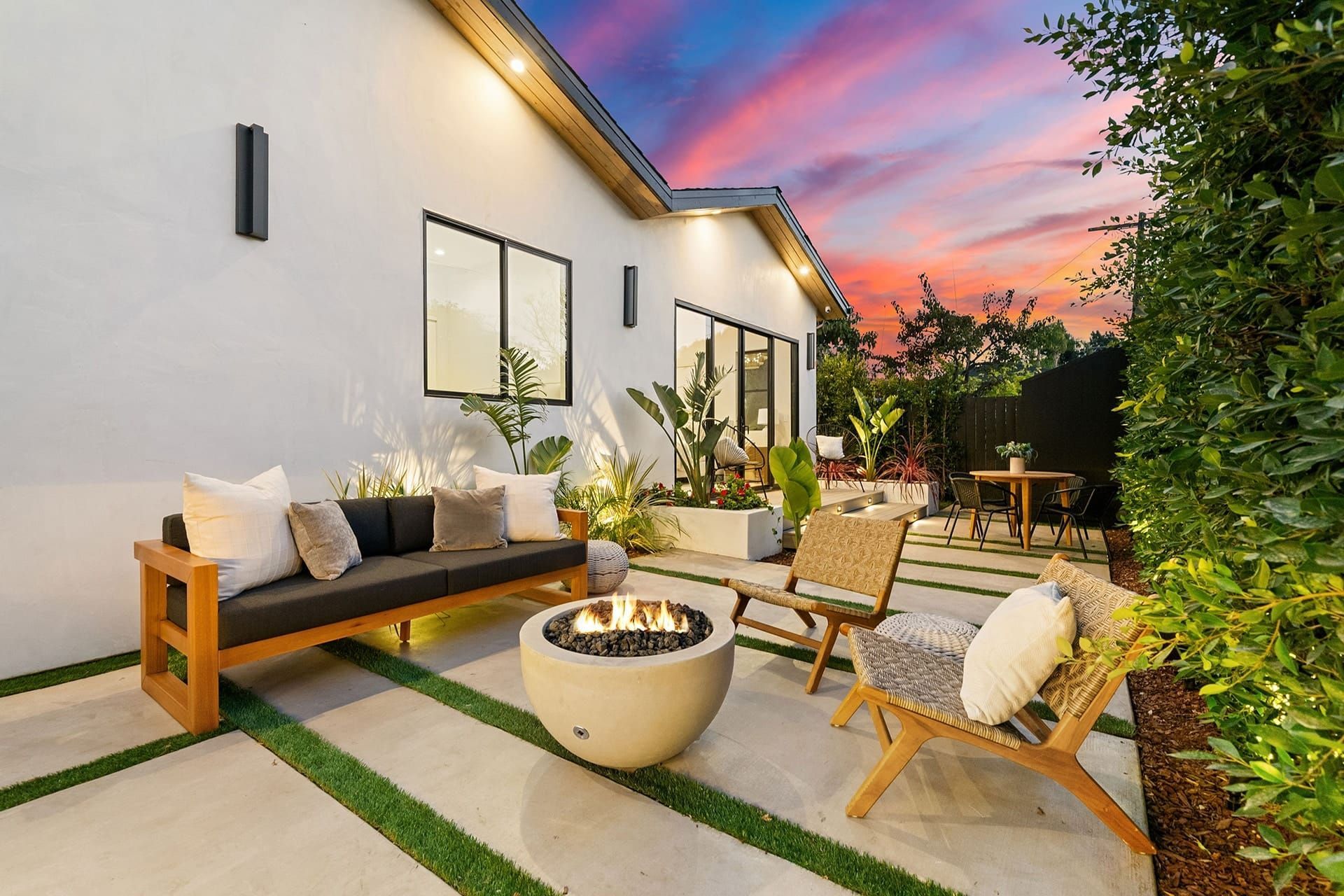 Modern patio with outdoor seating, fire pit, and sunset sky beside a white house
