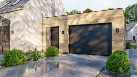 Modern beige house with a dark garage door, front entry, and landscaped shrubs in bright sunlight