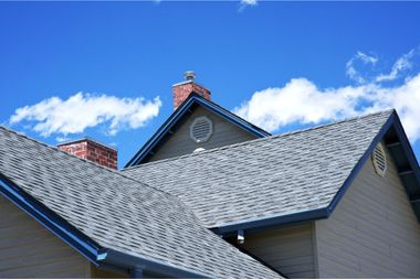 Gray shingled house roof against a bright blue sky with scattered clouds