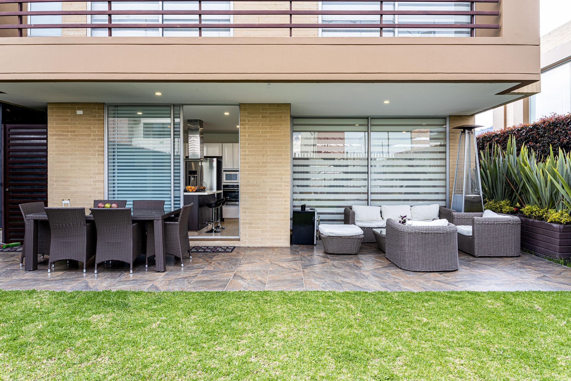 Outdoor patio with dining table, wicker seating, and a grassy lawn outside a modern house
