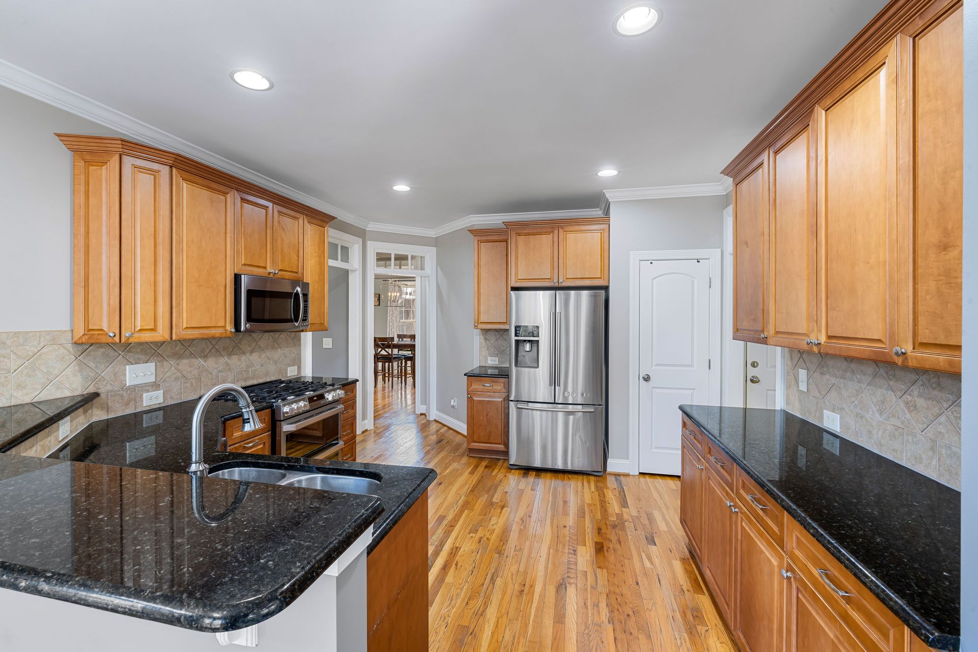 Bright kitchen with wood cabinets, black countertops, stainless steel appliances, and hardwood floors.