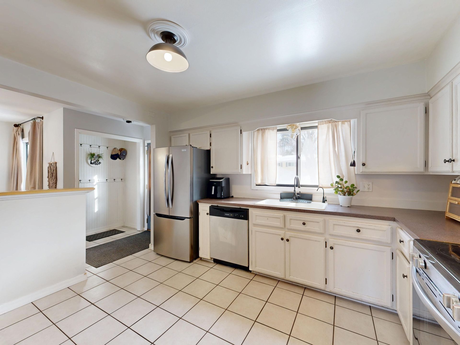 Bright white kitchen with stainless steel fridge, tiled floor, and a window over the sink