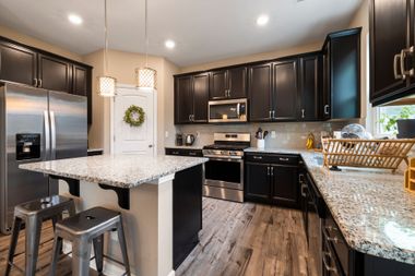 Modern kitchen with dark cabinets, stainless appliances, granite island, and wood-look flooring