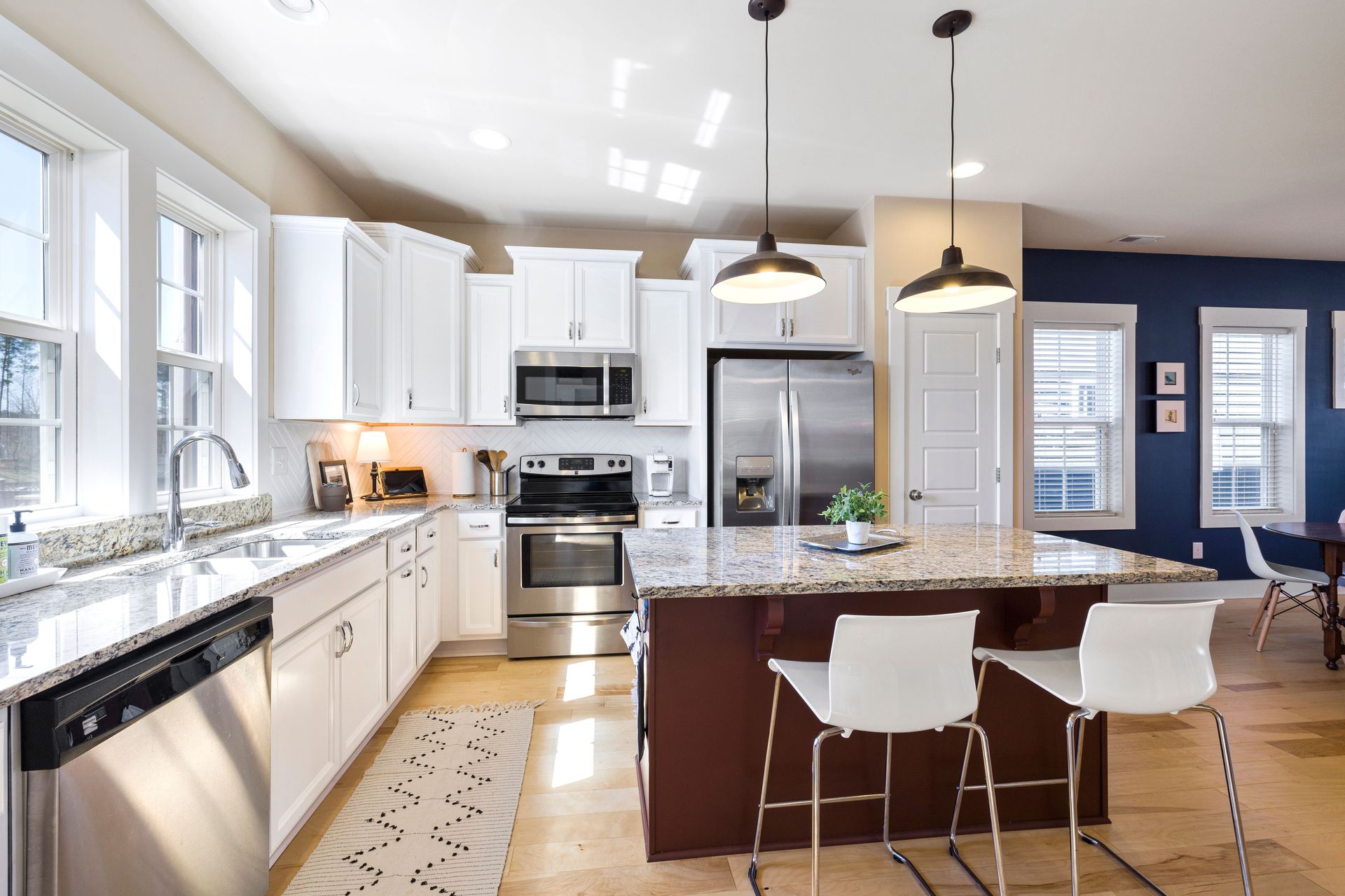 Bright modern kitchen with white cabinets, stainless appliances, blue accent wall, and island with bar stools