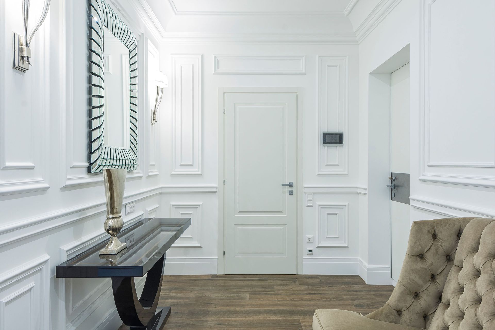 Elegant white hallway with paneled walls, console table, mirror, and tufted bench.