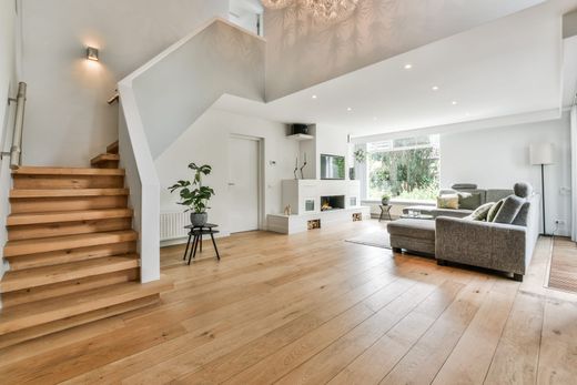 Bright modern living room with wood floors, gray sofa, staircase, and large windows