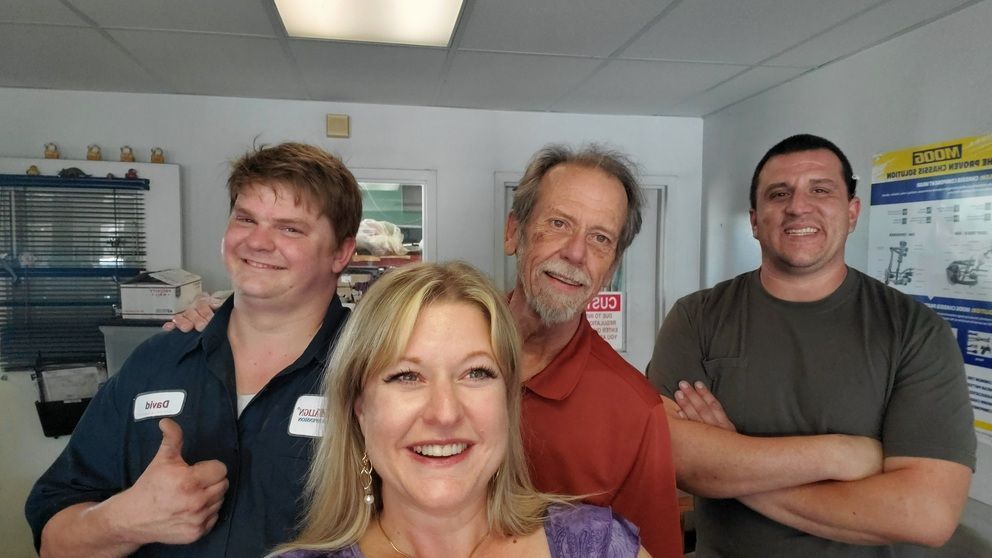 Four smiling people standing indoors in a room with shelves and fluorescent lights