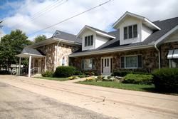 Stone house and garage with covered driveway on a quiet suburban street under a partly cloudy sky