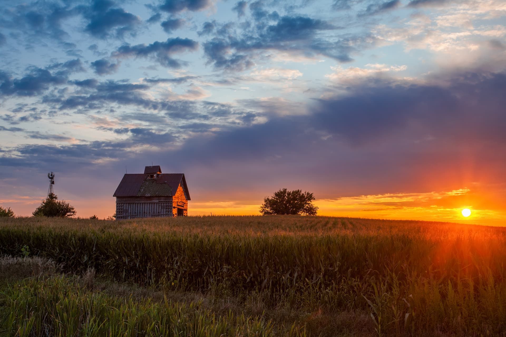 Sunset over a field with a small farmhouse and glowing orange horizon