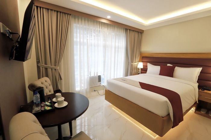 A hotel room with a king size bed , chair , table and television.