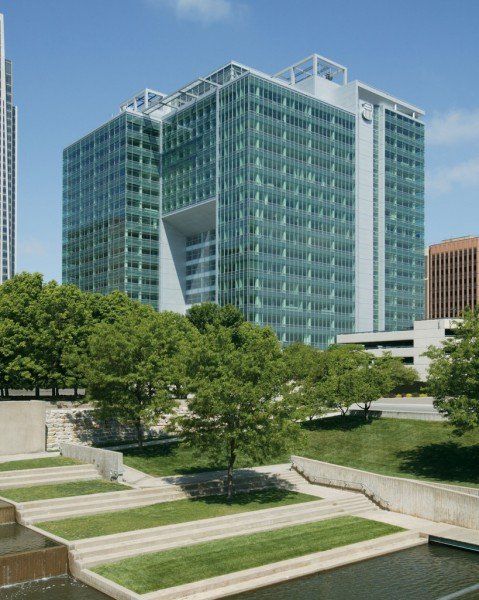 Modern glass office building with a rectangular cutout, surrounded by trees and tiered landscaping.