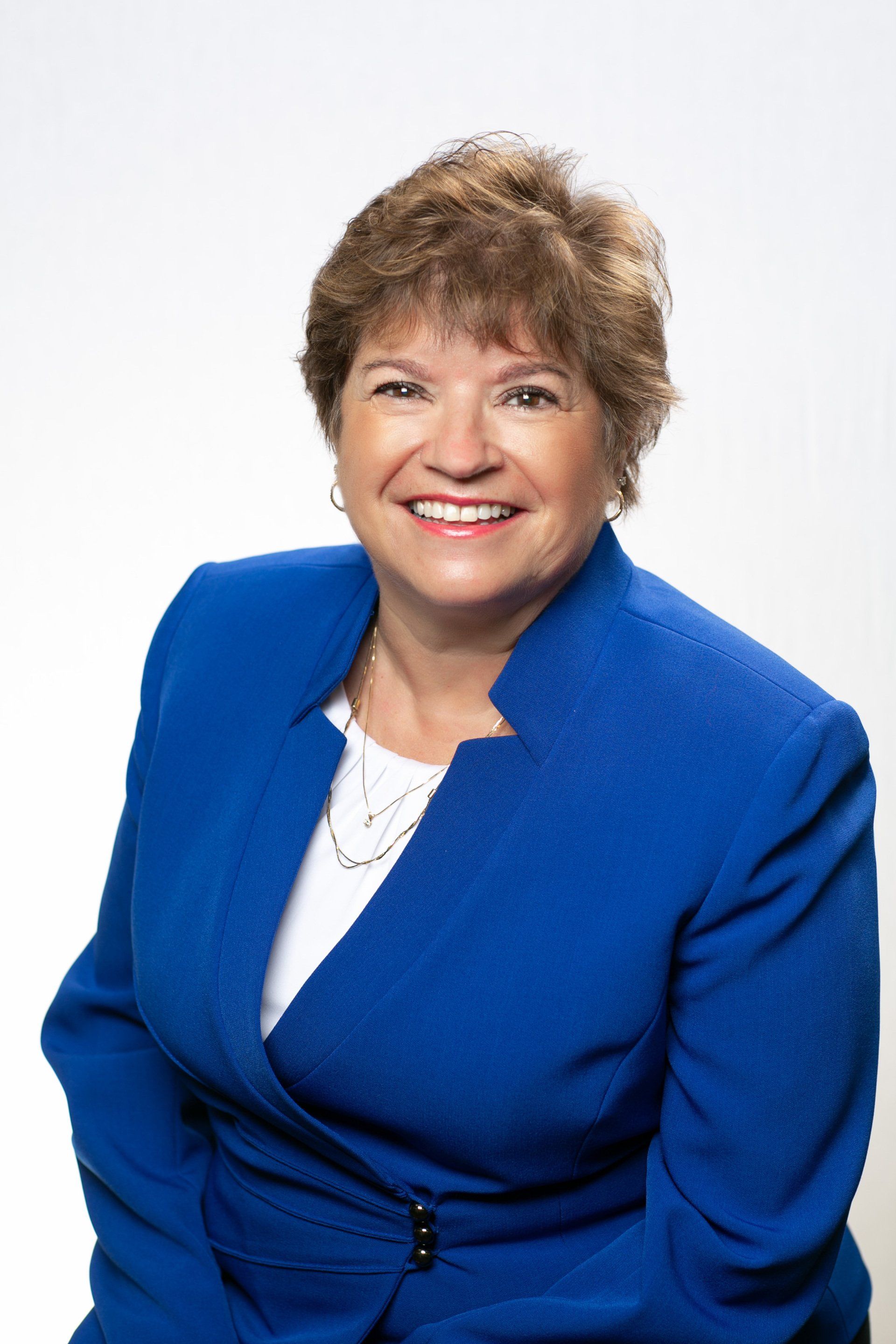 Woman with short brown hair wearing a blue blazer, smiling. White background.