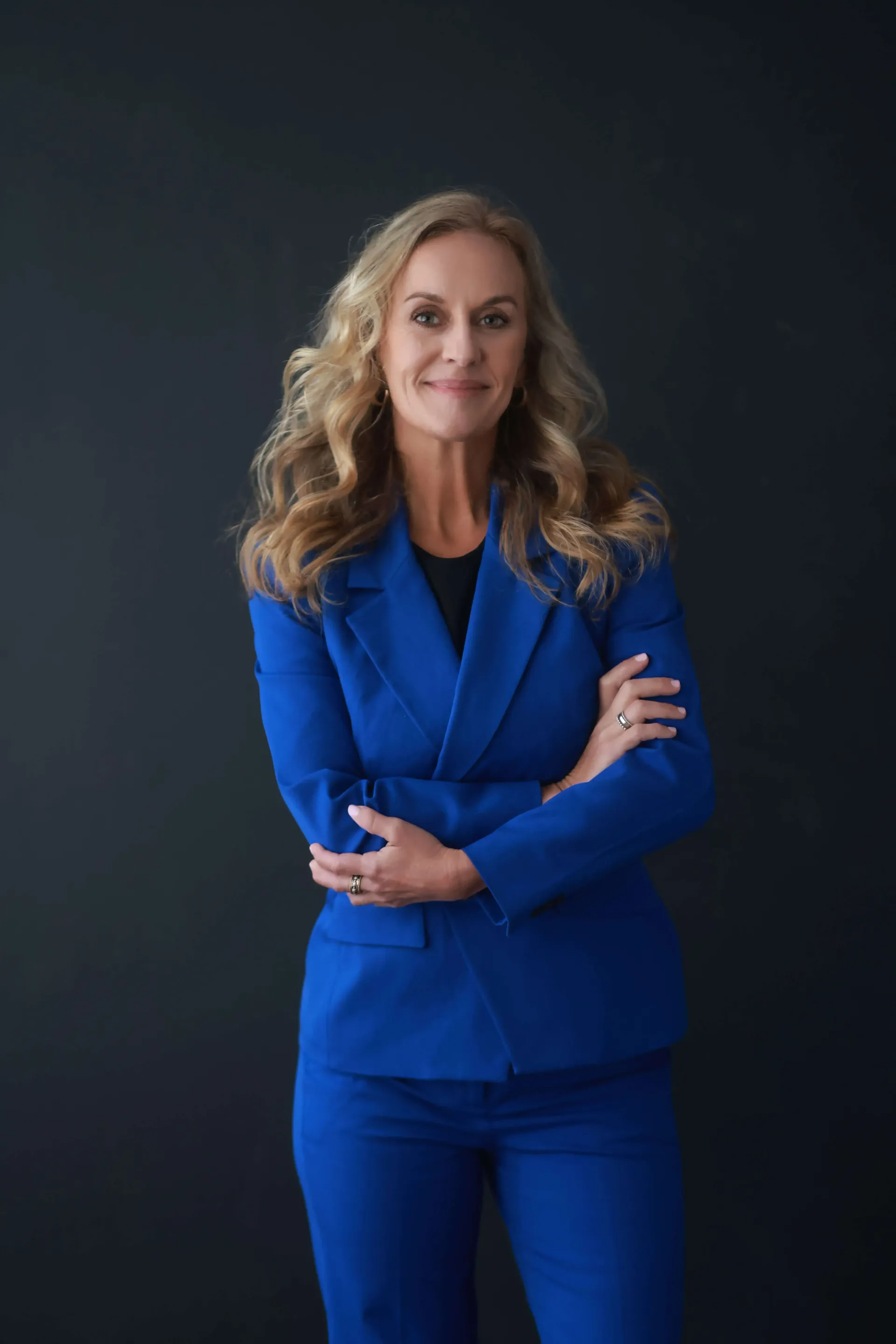 A woman in a blue suit is standing with her arms crossed.