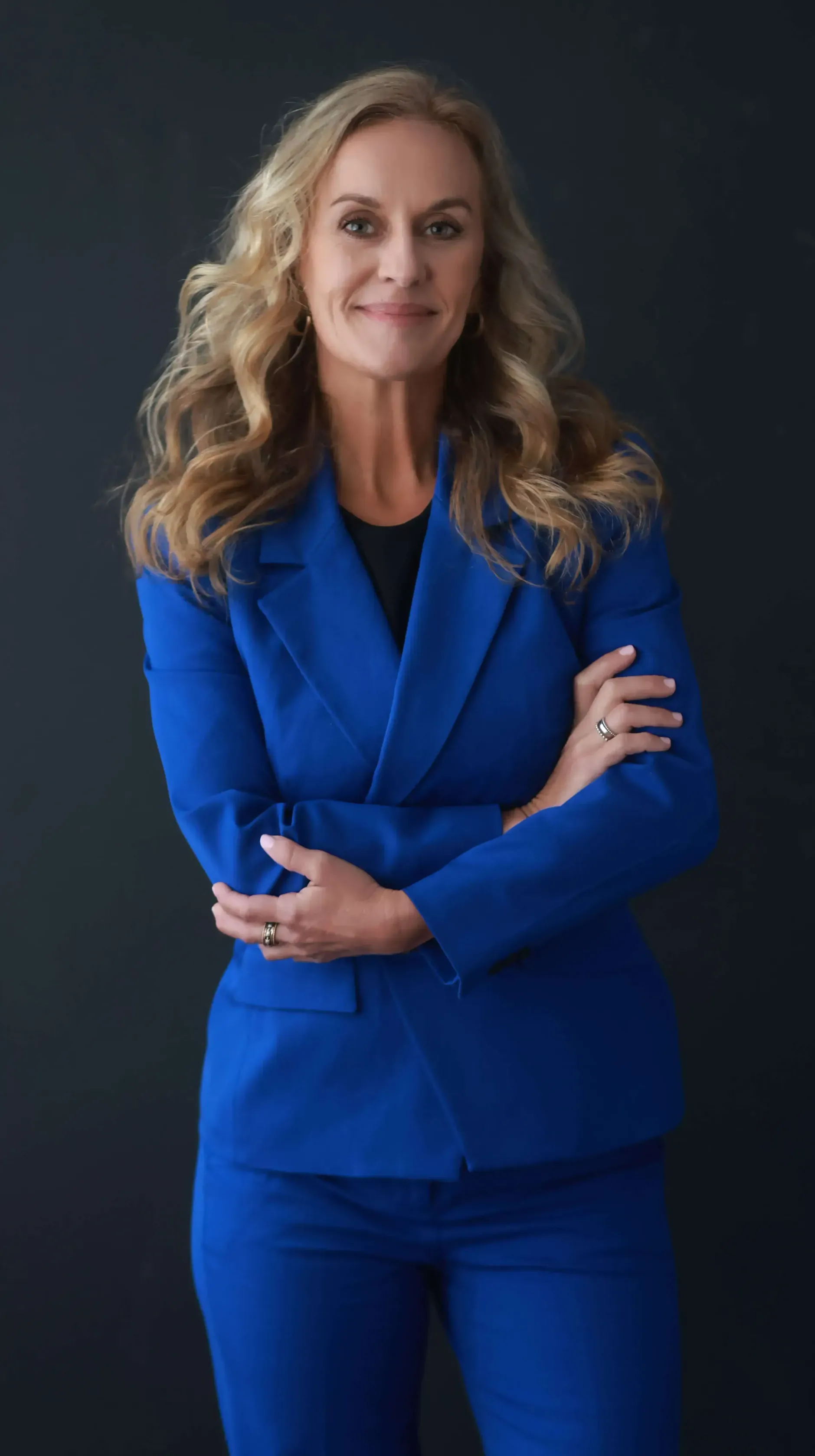 A woman in a blue suit is standing with her arms crossed.