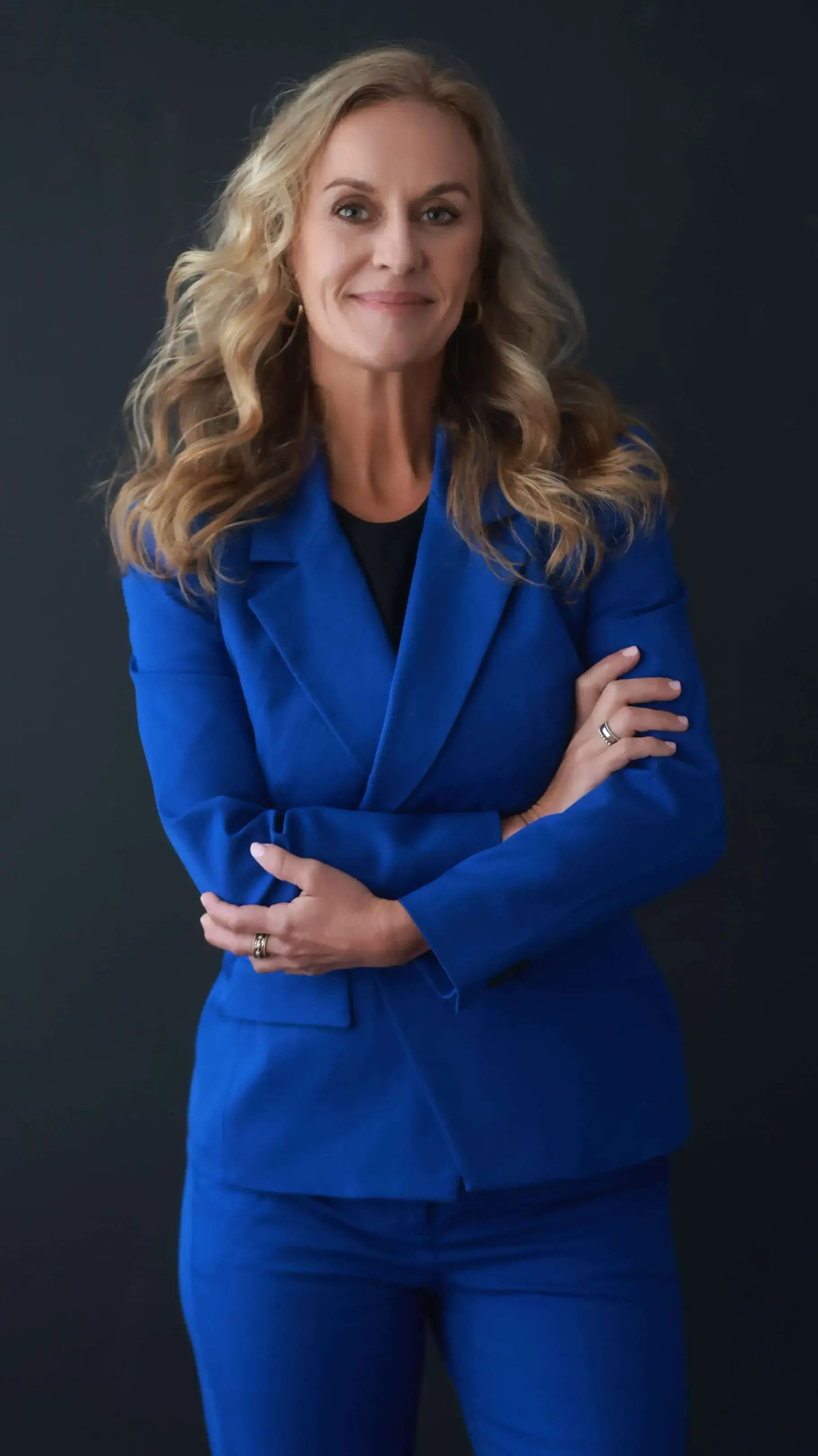 A woman in a blue suit is standing with her arms crossed.