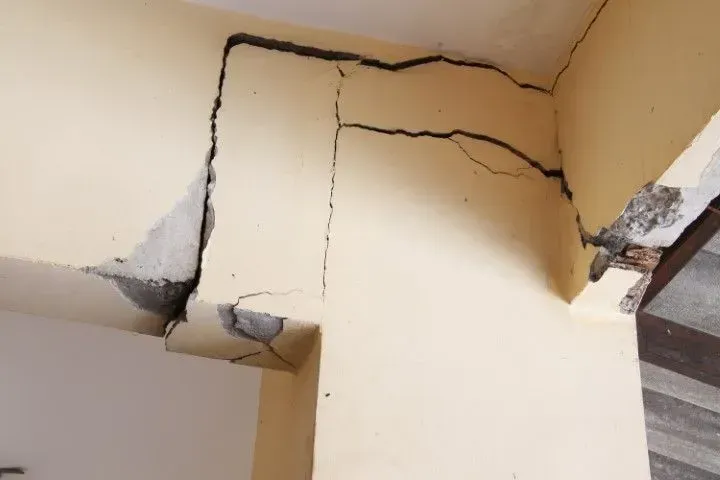 Cracked beige ceiling and wall corner with visible structural damage