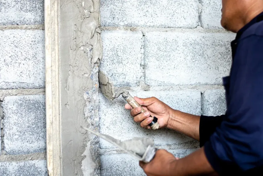 Worker applying plaster to a cinder block wall with a trowel