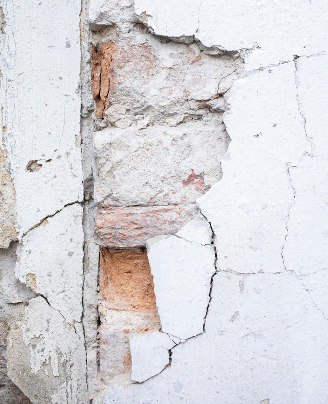 Cracked white wall with peeling plaster exposing red brick underneath