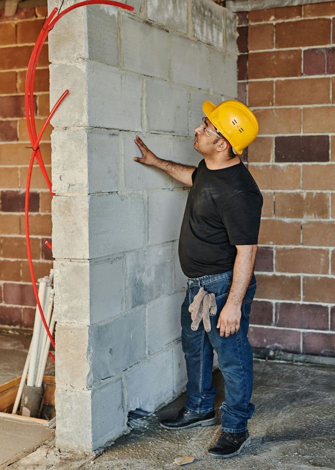 Worker in a hard hat inspecting a newly built cinder block wall indoors.