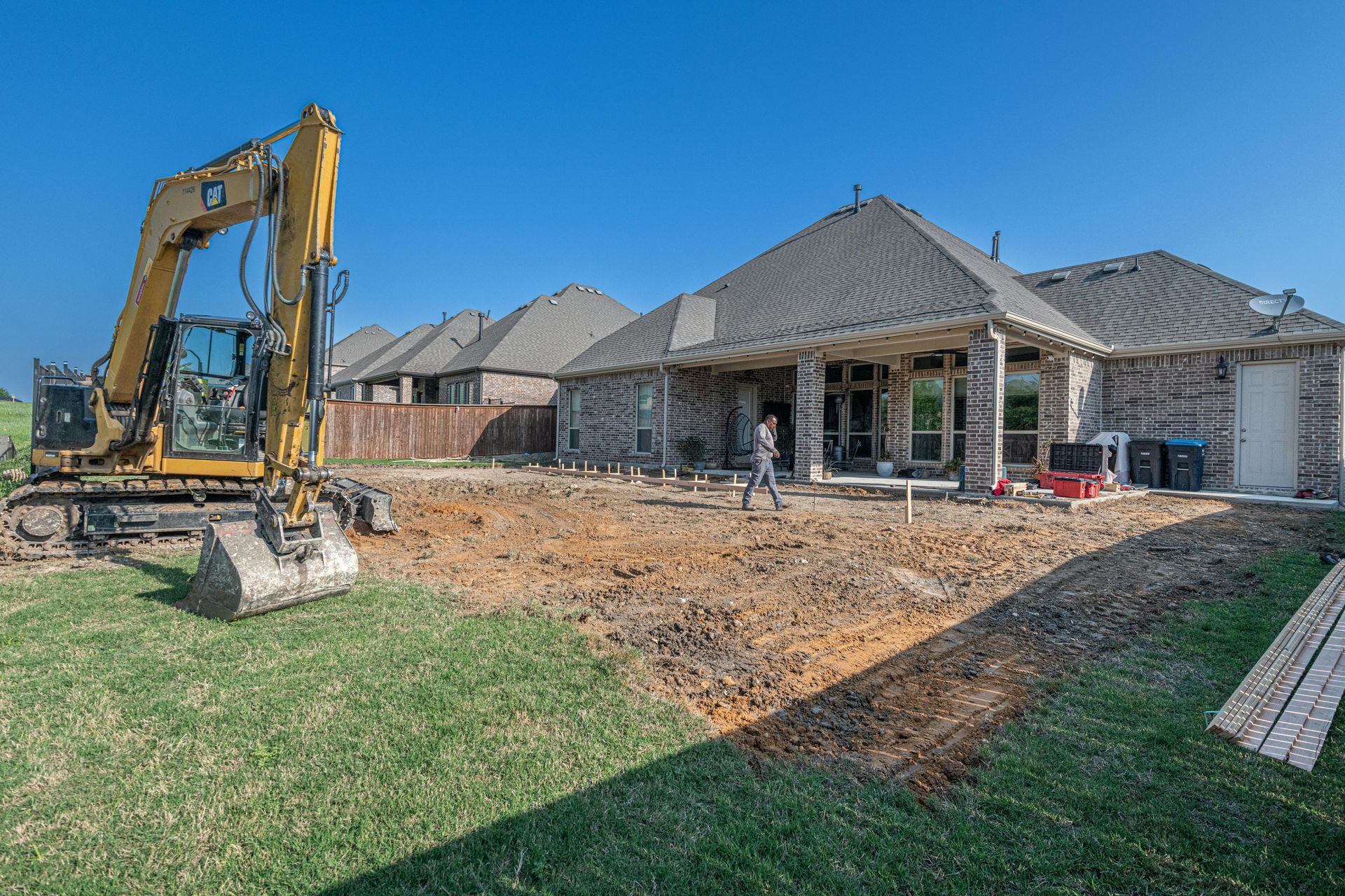 Yellow excavator at a house construction site with unfinished brick homes and dirt lot.