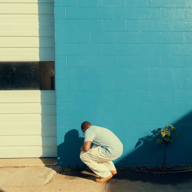 Person crouching beside a turquoise wall and white door in bright sunlight