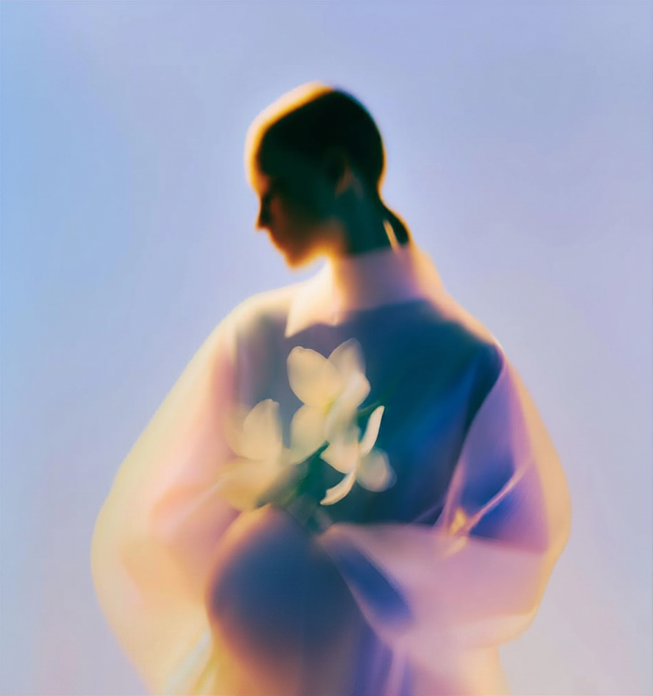 Blurred pastel portrait of a person in a blue top with white flower design against a soft lavender background