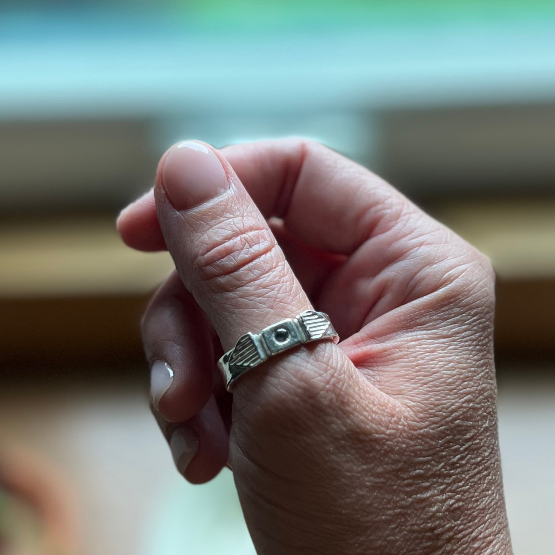 Silver ring with a raised design on a hand with pale skin. Wild Sunflower Silver Handmade Jewelry