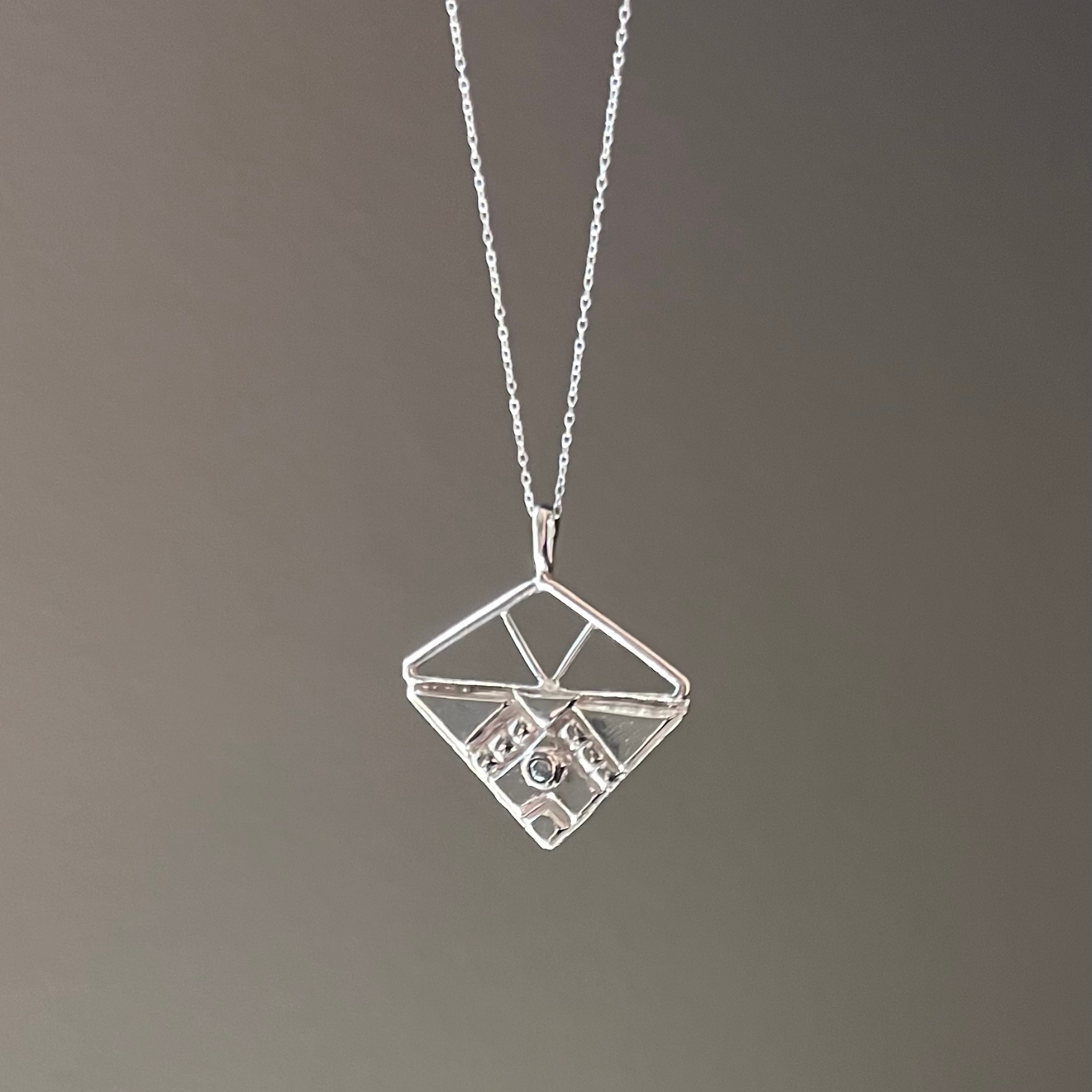 Silver geometric pendant necklace with small clear gems on gray backdrop. Wild Sunflower Silver Handmade Jewelry
