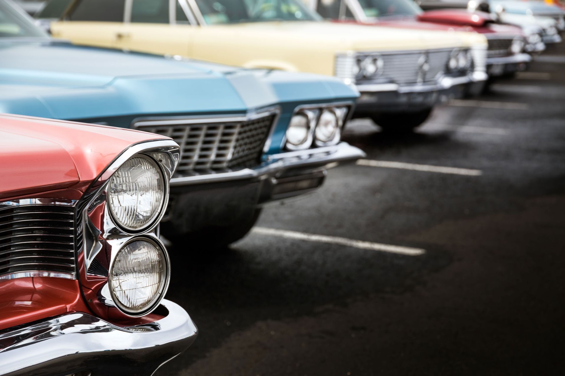 A row of old cars are parked in a parking lot.