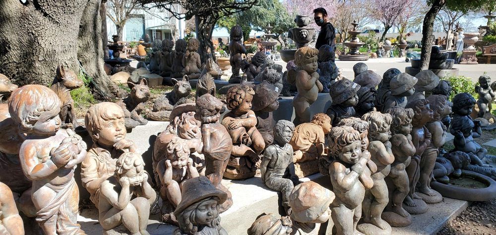 Rows of small stone statues displayed outdoors in a garden under trees.