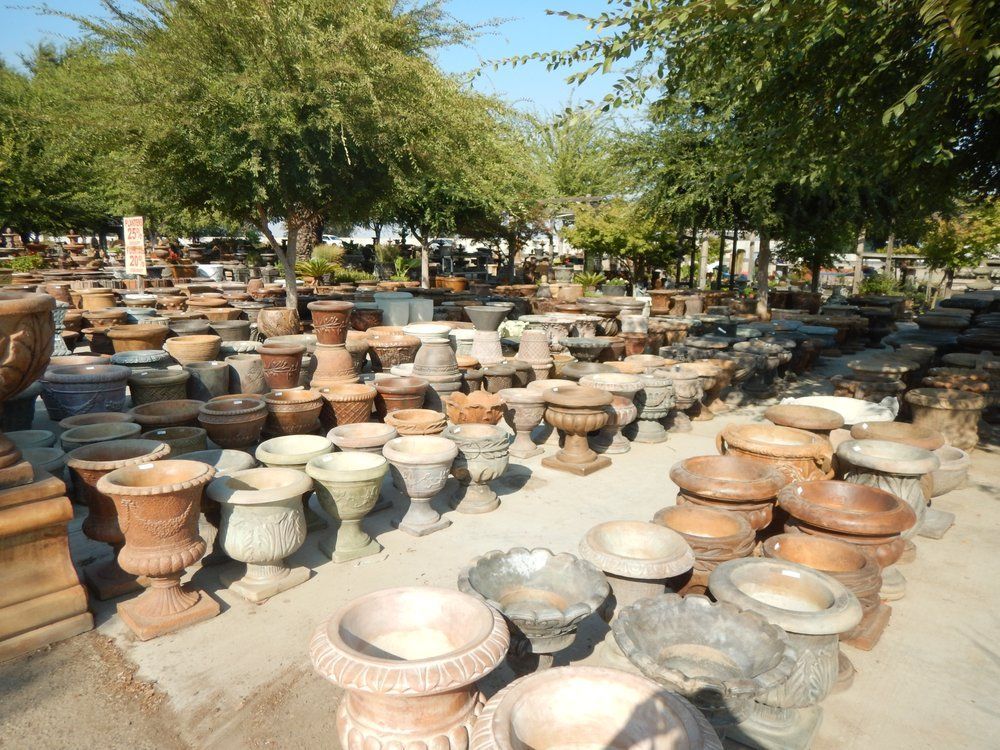 Rows of large clay pots and planters displayed outdoors under leafy trees in a market or workshop area