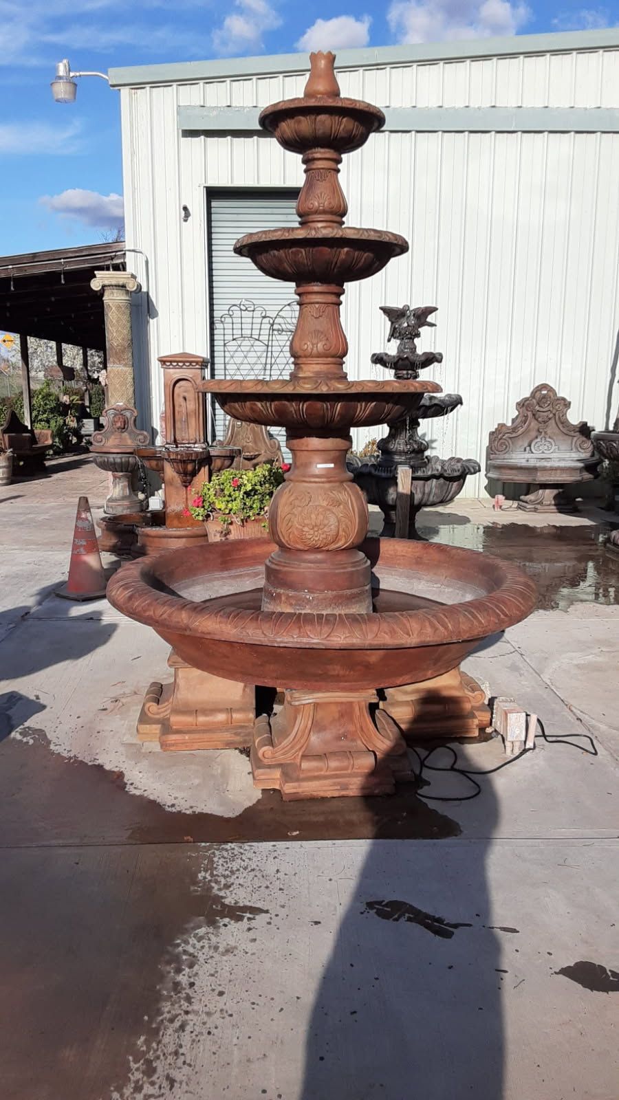 Rusty brown tiered outdoor fountain standing in front of a white building in a yard