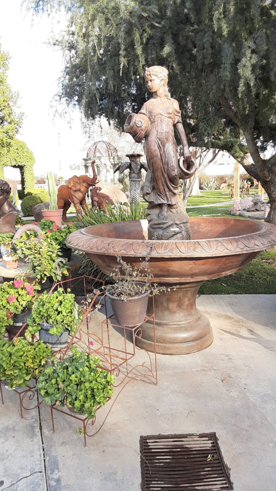 Bronze angel fountain in a garden courtyard with flowers and trees