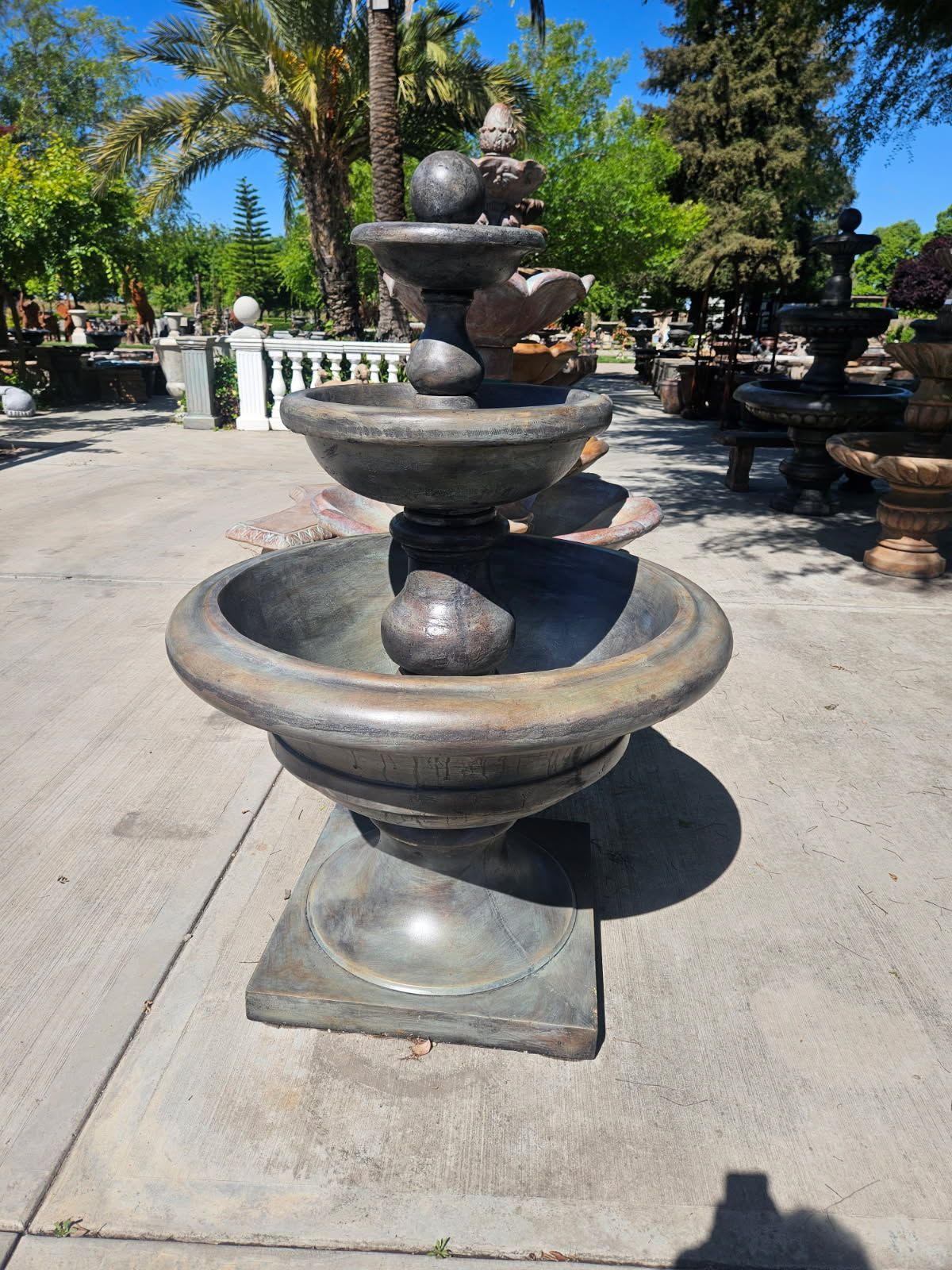 Stacked stone fountain sculpture in a sunny garden courtyard with palm trees and a concrete path
