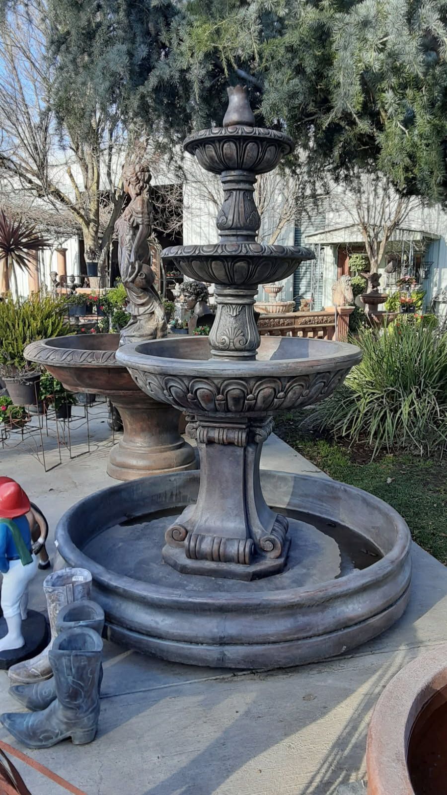 Tiered stone fountain in a garden courtyard, with decorative urns and greenery around it.