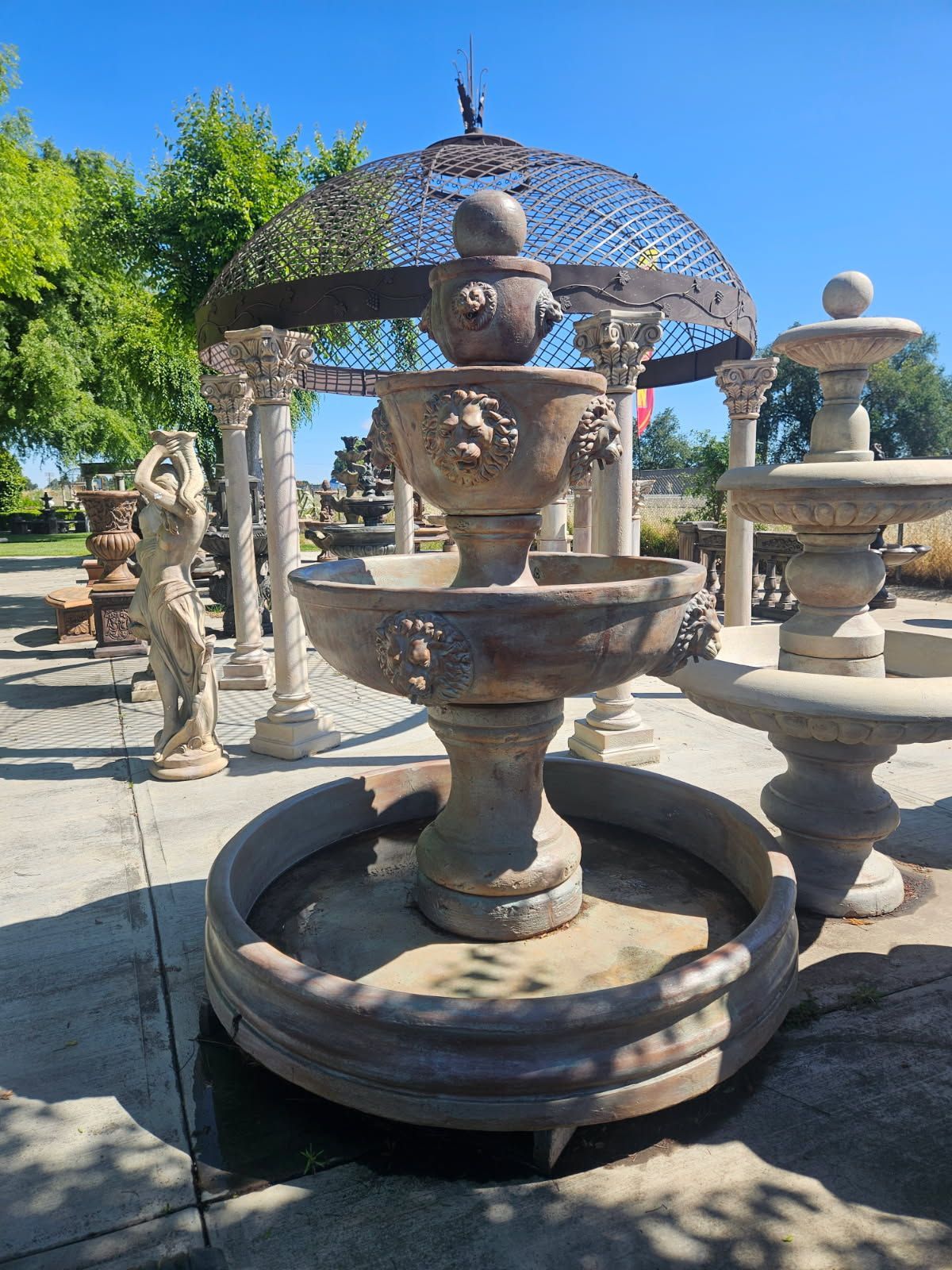 Outdoor stone fountain with stacked urns and a domed metal sculpture in a sunny garden courtyard