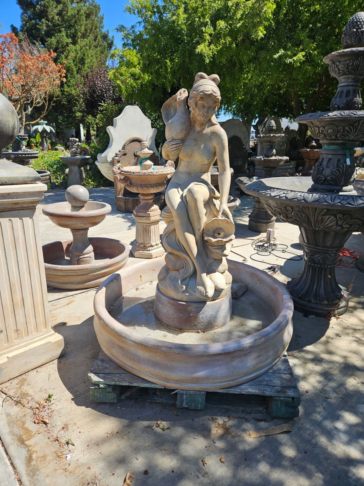 Outdoor stone fountain with a cherub statue in a garden, surrounded by other fountains and trees