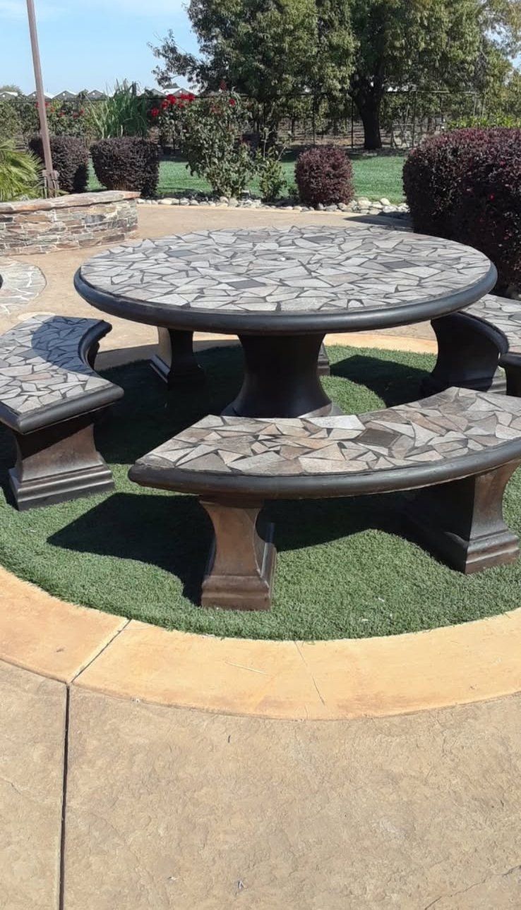 Round stone picnic table with curved benches on a grassy outdoor patio