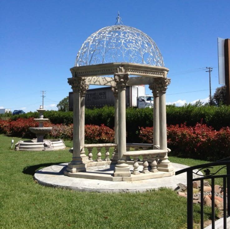 White gazebo with a domed lattice roof in a landscaped park under a clear blue sky