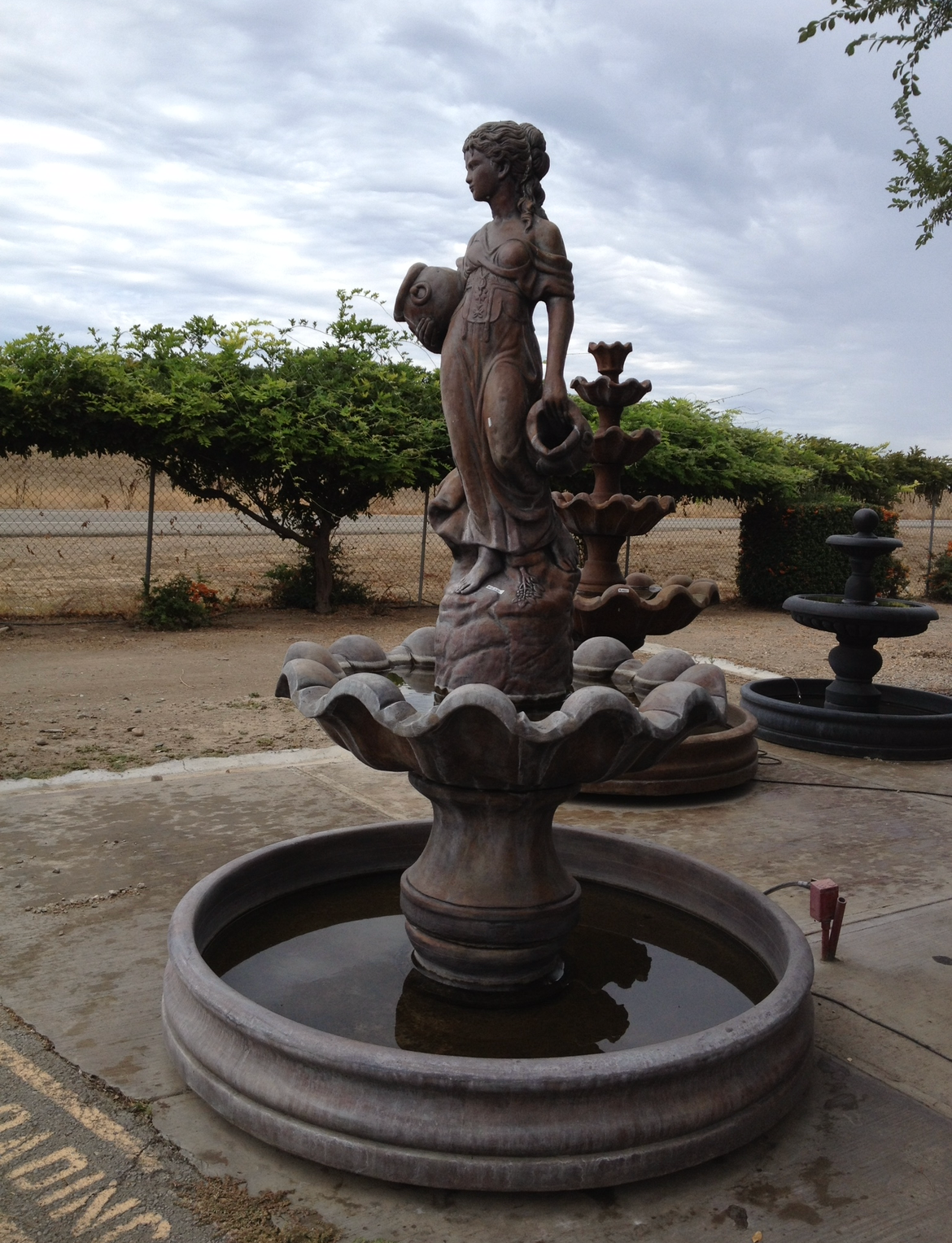 Stone fountain with a female statue in a garden courtyard under cloudy sky