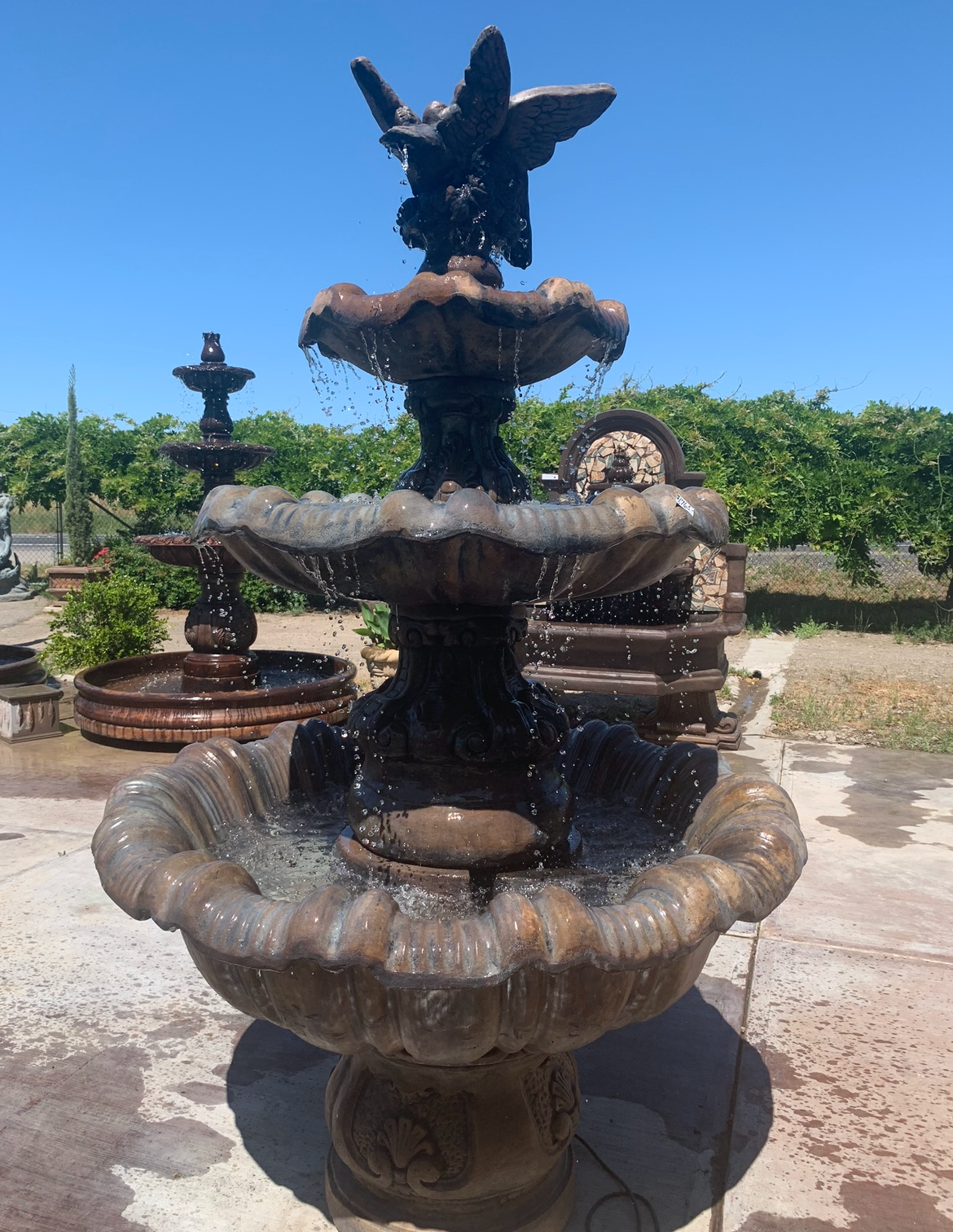 Outdoor tiered stone fountain with sculpted birds on top, in a sunny garden setting