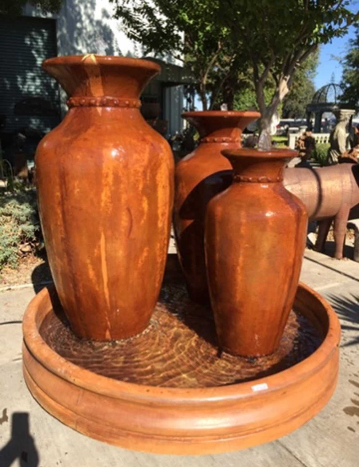 Three orange terracotta vases in a round planter outdoors.