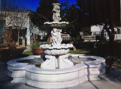 White tiered fountain in a courtyard with trees and buildings in the background