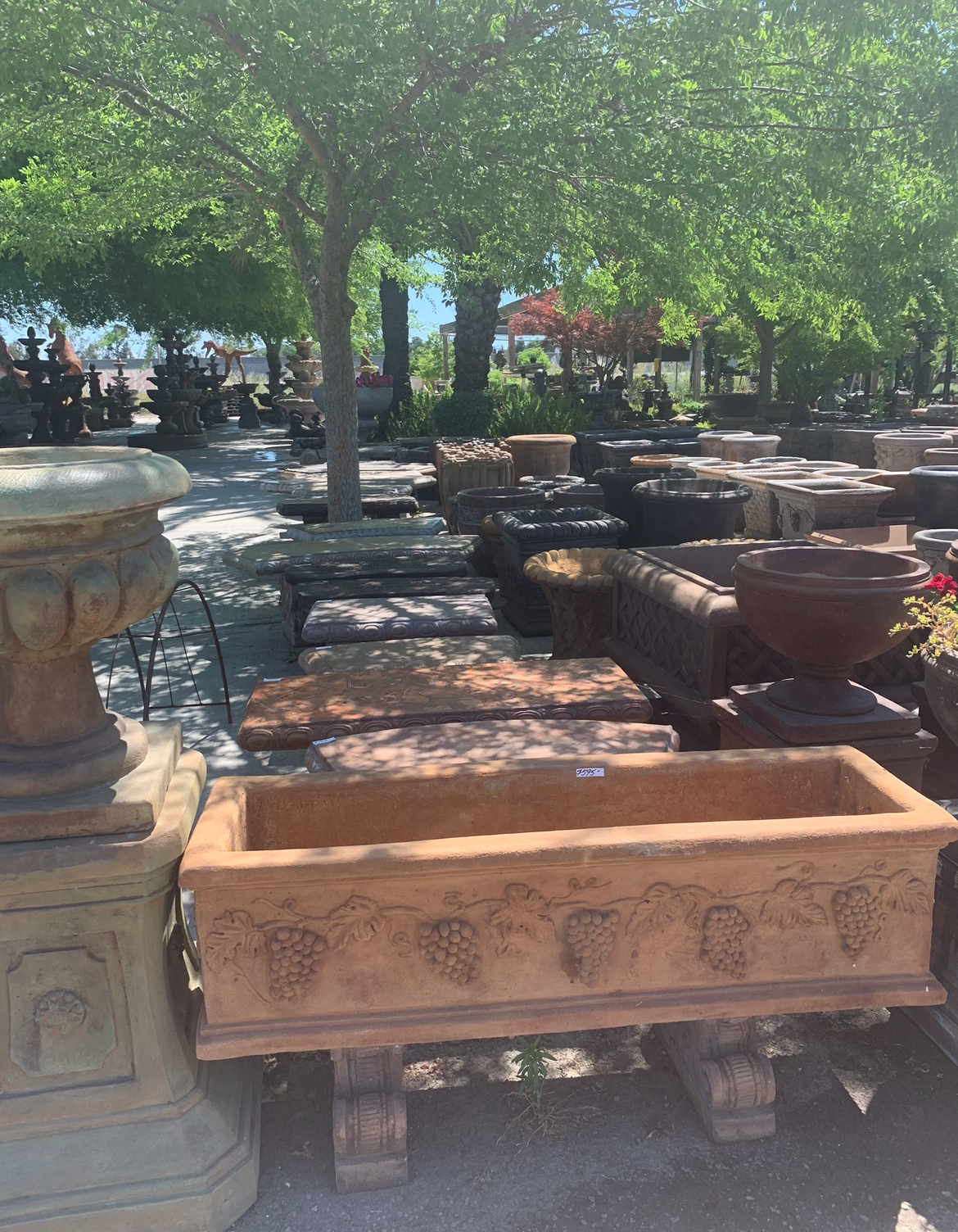 Rust-colored stone planters displayed outdoors under trees in a sunny garden