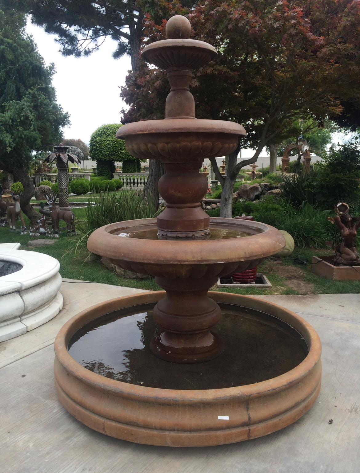 Terracotta tiered fountain in a garden, with water in the basin and trees in the background