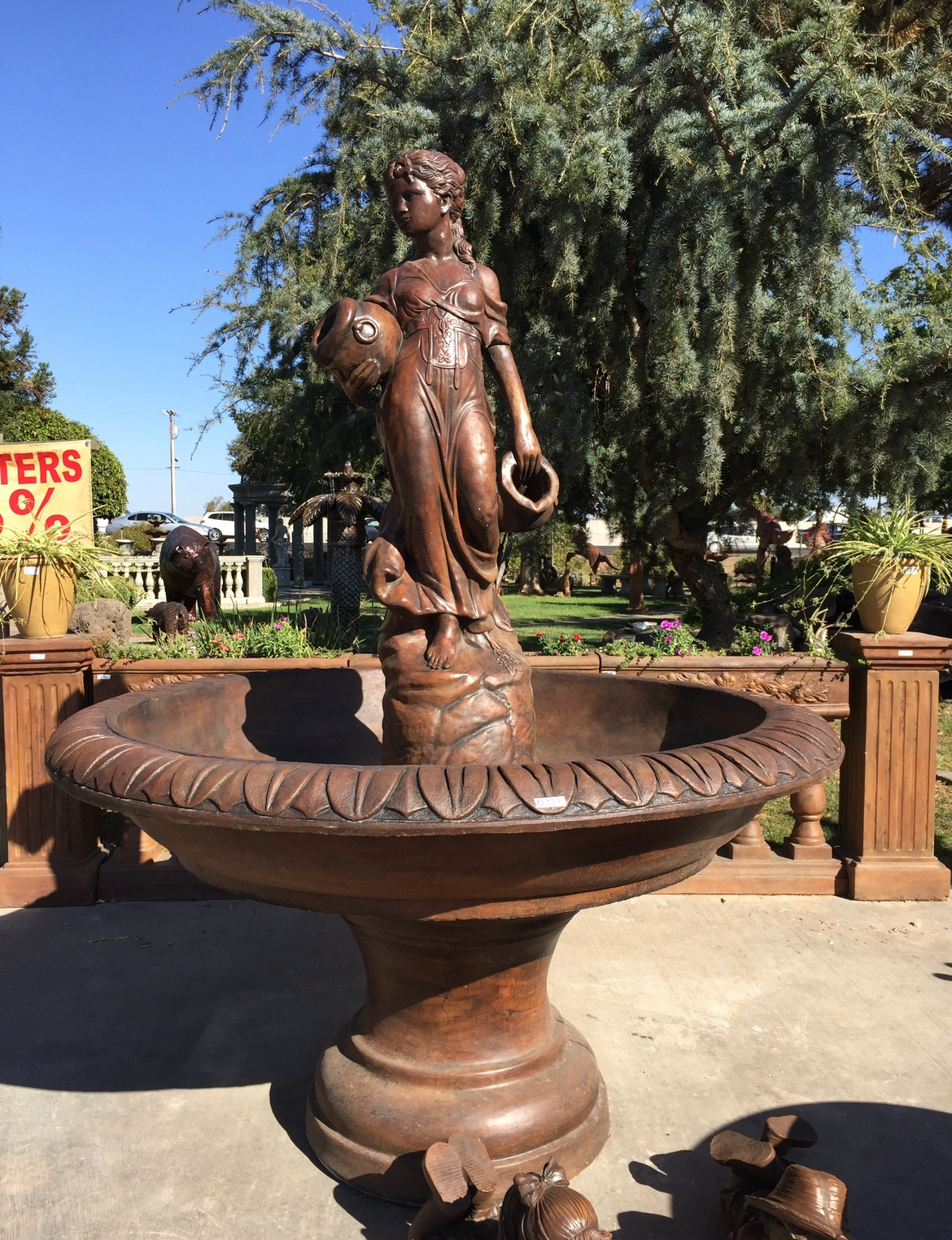 Bronze statue fountain in a sunny outdoor garden courtyard, with trees and benches in the background